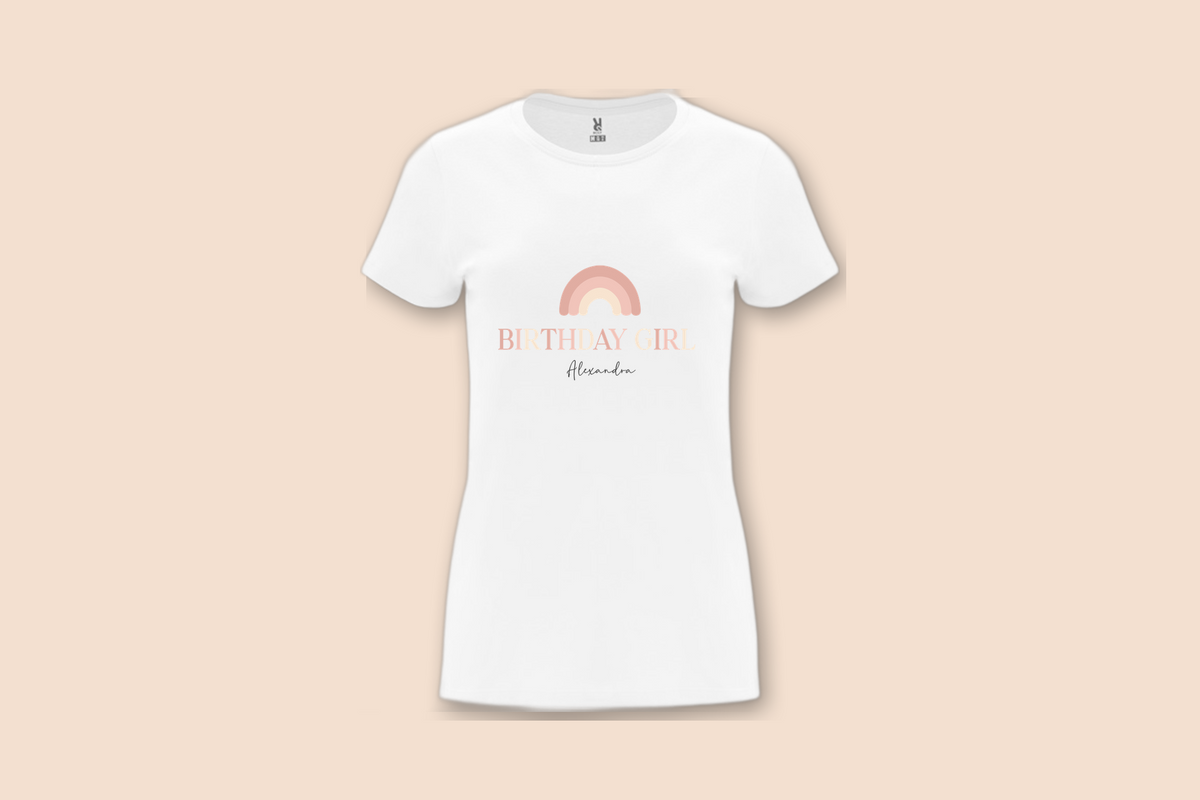 A white "The Pinks" Birthday Girl Rainbow Tee with a personalized name displayed on a plain background.