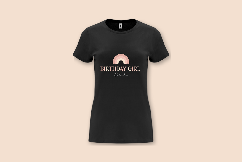 A black "The Pinks" Birthday Girl Rainbow Tee with a personalized name displayed on a plain background.