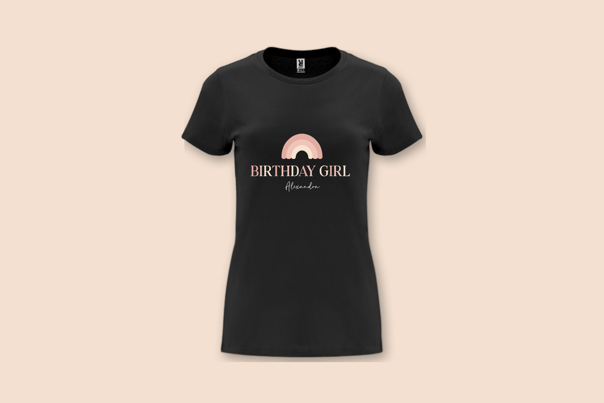 A black "The Pinks" Birthday Girl Rainbow Tee with a personalized name displayed on a plain background.